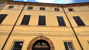 A building with a yellow facade, multiple windows with shutters, and an arched entrance. - Petrucci House 2 historic center (Forlì)