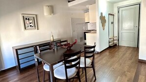 A dining area with a wooden table and chairs, a white wall with a framed picture, and a kitchen in the background. - Petrucci House 2 historic center (Forlì)