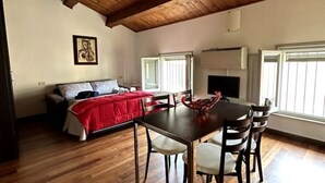 A cozy room with a wooden ceiling, a bed with a red blanket, a dining table with chairs, and a TV on the wall. - Petrucci House 2 historic center (Forlì)