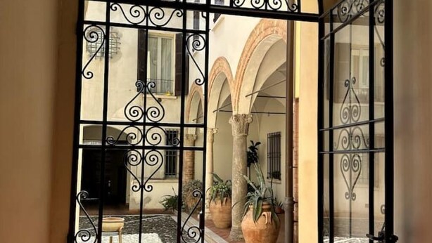 An open wrought iron gate leading to a courtyard with arches, potted plants, and a tiled floor. - Petrucci House 2 historic center (Forlì)