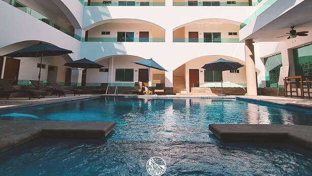 A hotel pool area with multiple levels of balconies, lounge chairs, and umbrellas. - Hotel TamYanJa (Tamiahua)
