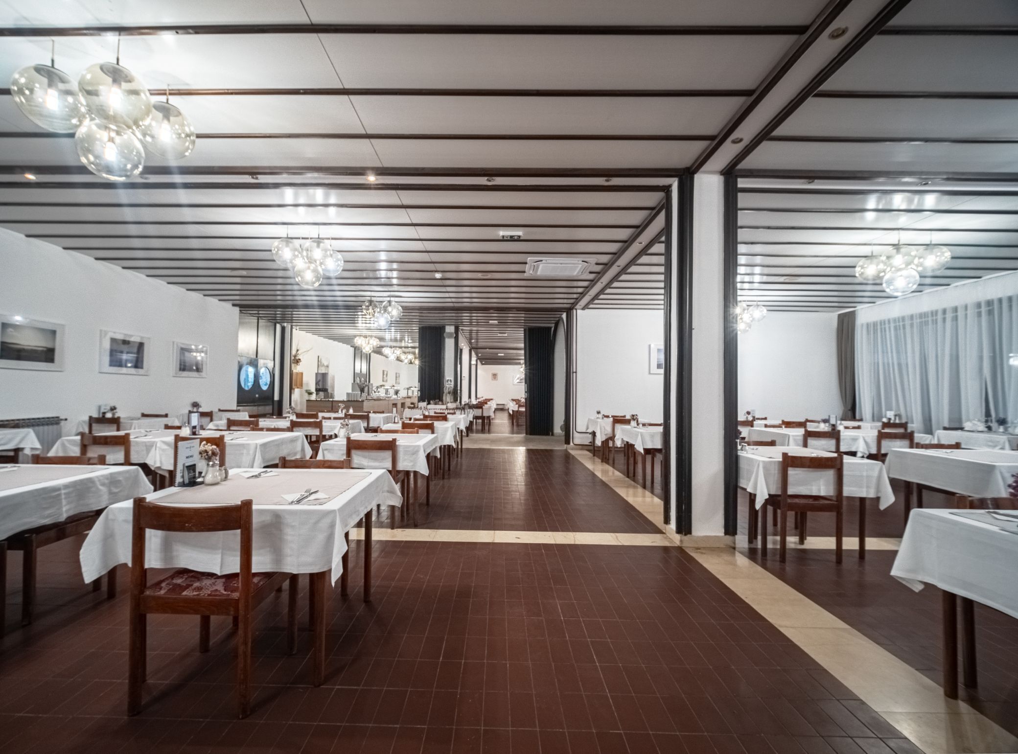 A spacious dining area with multiple tables and chairs, a central walkway, and modern lighting fixtures.