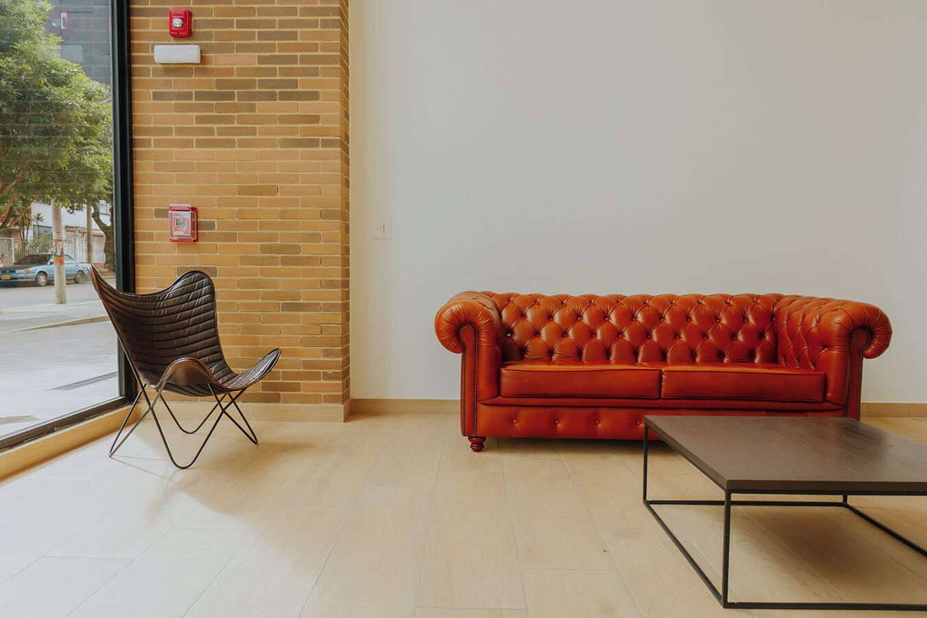 A room with a brick wall, a leather sofa, a cushioned chair, and a wooden table.