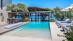 Ett poolområde med en pergola, solstolar och utsikt över havet.