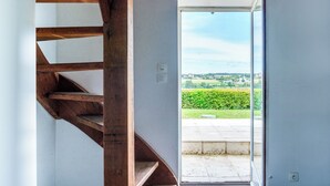 Een houten trap leidt naar een deur met een ruit, met uitzicht op een groen landschap en een geplaveid gebied.