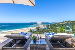 A balcony with wicker furniture, a glass table, and a view of the beach and ocean. - Villa Rice - Eight Bedroom Villa, Sleeps 16 (Plettenberg Bay)