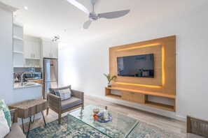 Un salon moderne avec un téléviseur à écran plat fixé à un mur en bois, une table basse en verre, un canapé et un ventilateur de plafond.