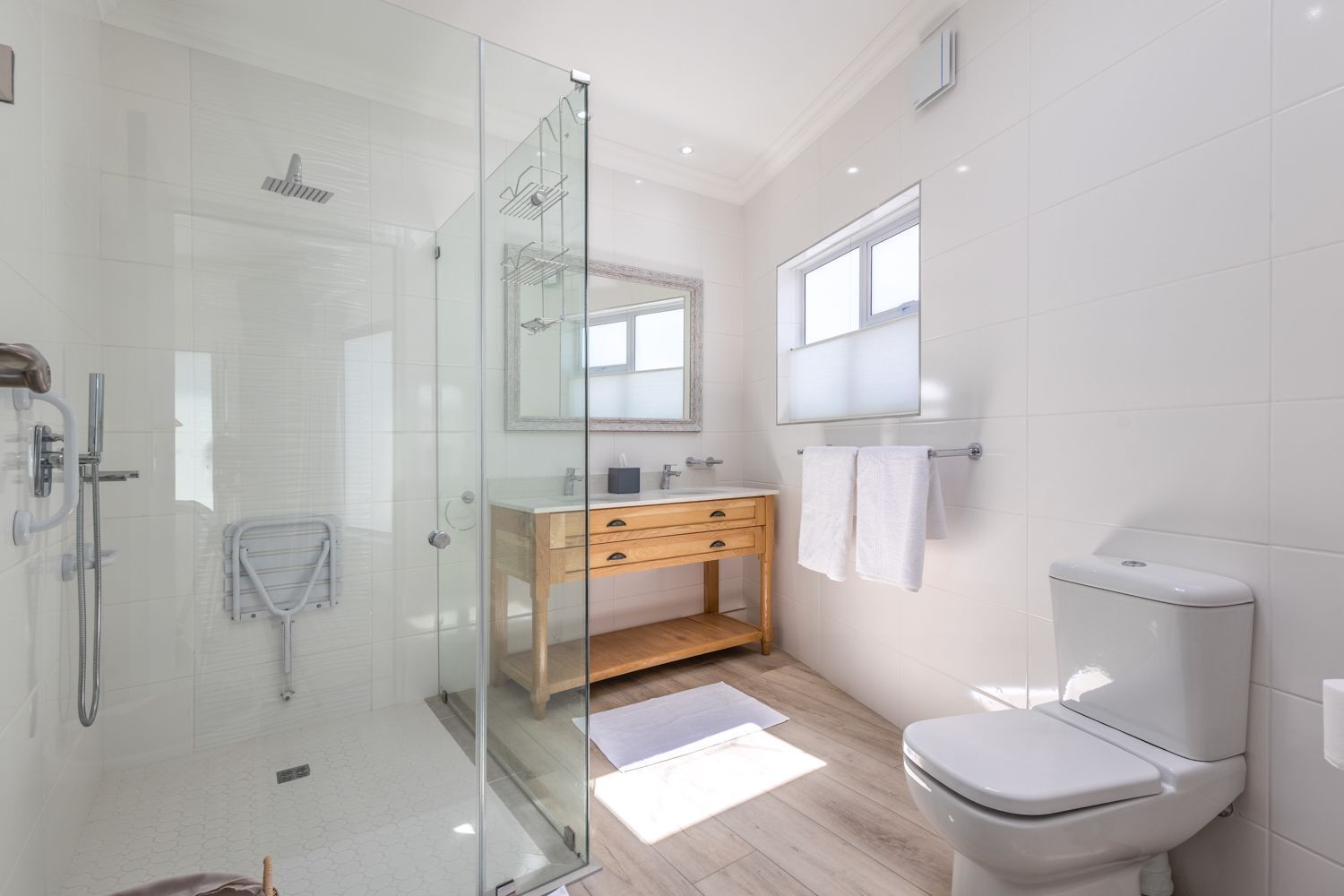 Une salle de bain moderne avec une douche à parois de verre, un meuble-lavabo en bois, des toilettes et un grand miroir.
