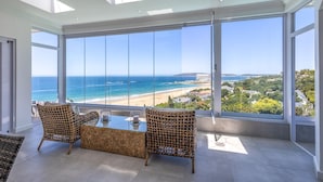 A room with large windows overlooking a beach, wicker furniture, and a clear view of the ocean. - Villa Rice - Eight Bedroom Villa, Sleeps 16 (Plettenberg Bay)