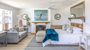 A bedroom with a bed, a sofa, a fireplace, a ceiling fan, and a large mirror. - Villa Rice - Eight Bedroom Villa, Sleeps 16 (Plettenberg Bay)