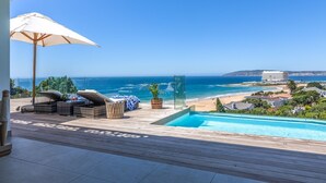 A poolside area with a view of the ocean, lounge chairs, and a glass-enclosed pool. - Villa Rice - Eight Bedroom Villa, Sleeps 16 (Plettenberg Bay)