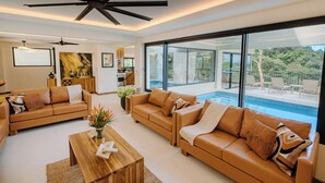 A modern living room with leather sofas, a wooden coffee table, and a large window overlooking a pool and outdoor seating area.