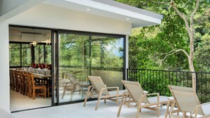 A modern outdoor dining area with glass doors, wooden chairs, and a table set for a meal.