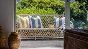 A wicker sofa with striped cushions, positioned on a balcony with a view of lush greenery and hills.