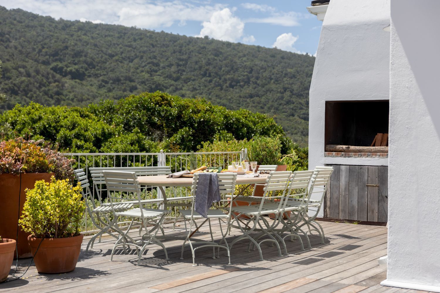 An outdoor patio with a table and chairs, surrounded by potted plants.