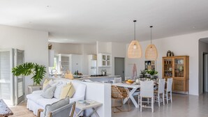 A modern living room with a white sofa, dining table, and chairs. There is a kitchen area with white cabinets and a dining table.