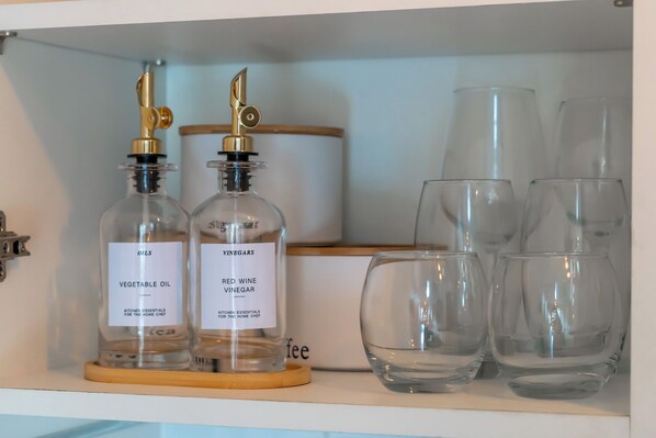 A kitchen shelf with two glass bottles labeled 'Vegetable Oil' and 'Red Wine Vinegar', and several clear glass cups.