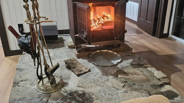 Une pièce au sol dallé de pierres, avec un poêle à bois, un poêle en fonte de style ancien, et une porte sur le côté droit.