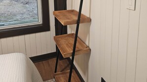 Une petite pièce comprenant un lit, une fenêtre et une étagère en bois fixée au mur.