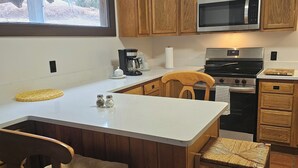 Une cuisine dotée de meubles en bois, d’un four à micro-ondes en acier inoxydable, d’une machine à café et d’un grand îlot central avec deux chaises.