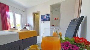 Et hotelværelse med en seng, et fjernsyn, et glasbord med en drink, en kop og en vase med blomster.