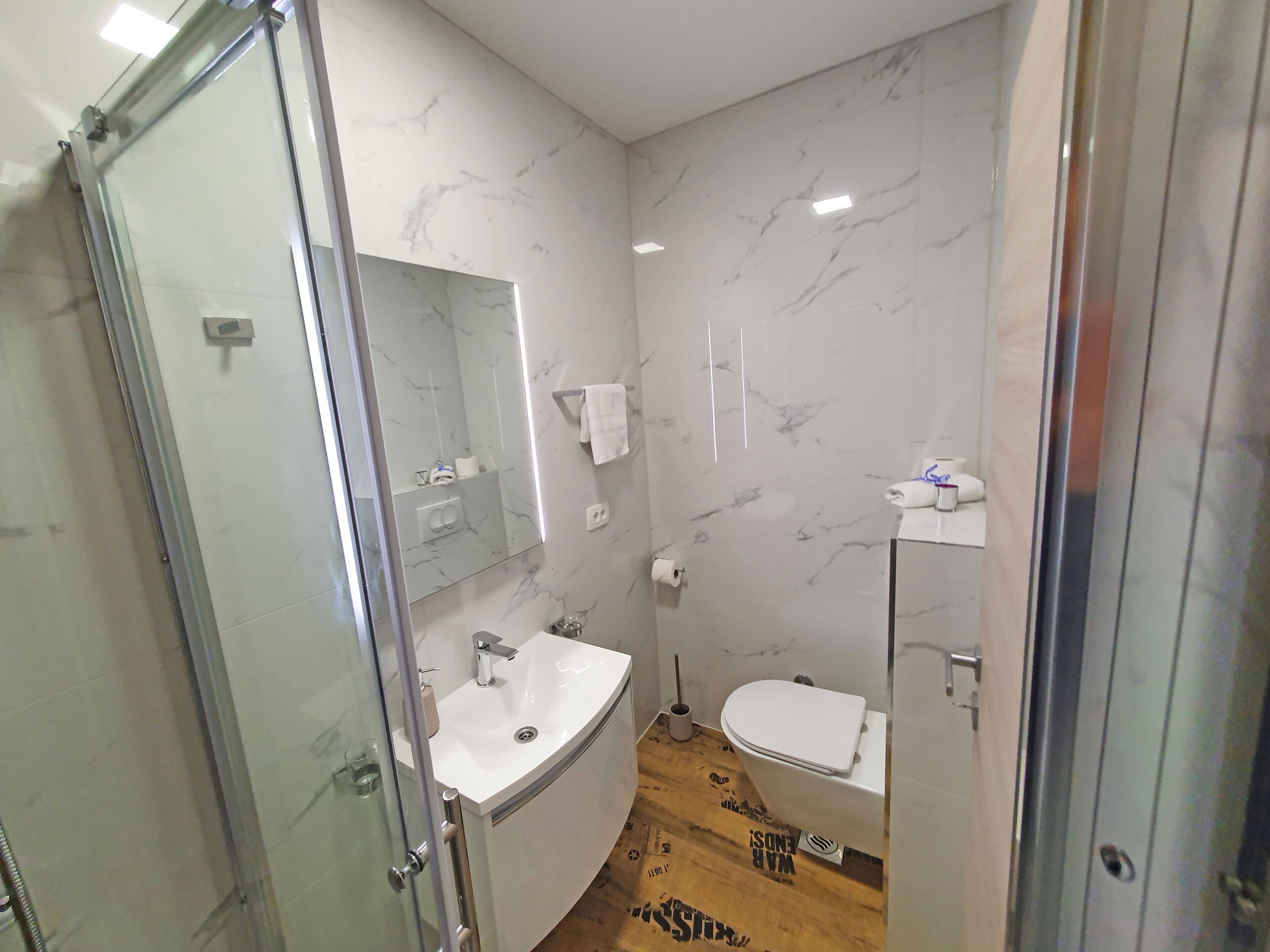 Ein modernes Badezimmer mit Duschabtrennung aus Glas, einem weißen Waschbecken und einer Toilette.