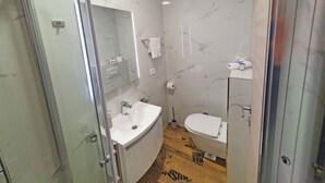 Et moderne badeværelse med glasvæg omkring brusebad, en hvid vask og et toilet.