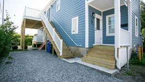 A two-story house with a front porch, a staircase leading to the upper floor, and a small front yard with gravel.
