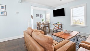 A modern living room with a brown leather sofa, wooden coffee table, and a flat-screen TV mounted on the wall.