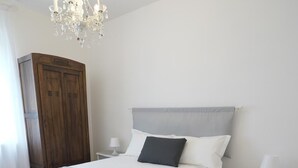 Et soveværelse med en stor seng, et træskab, en lysekrone og et sengebord med en lampe.