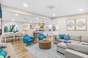 A spacious living area with a neutral color palette, a kitchen in the background, and a dining area with a table and chairs.