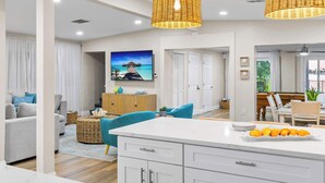 A modern kitchen with white cabinetry, a central island, and a dining area with a wooden table and chairs. - 4 Master Suites, Heated Pool, Game Room, King Beds (Indian Rocks Beach)