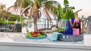 A table with a bowl of fruit, a bottle of champagne, and a basket with a bottle of sauce. - 4 Master Suites, Heated Pool, Game Room, King Beds (Indian Rocks Beach)
