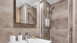 A modern bathroom with a large mirror, a white sink, and a glass shower enclosure. - Cozy Studio in Central Locale with Kitchenette (London)