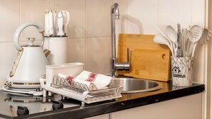 A kitchen with a kettle, dish rack, utensils, and a wooden cutting board. - Cozy Studio in Central Locale with Kitchenette (London)