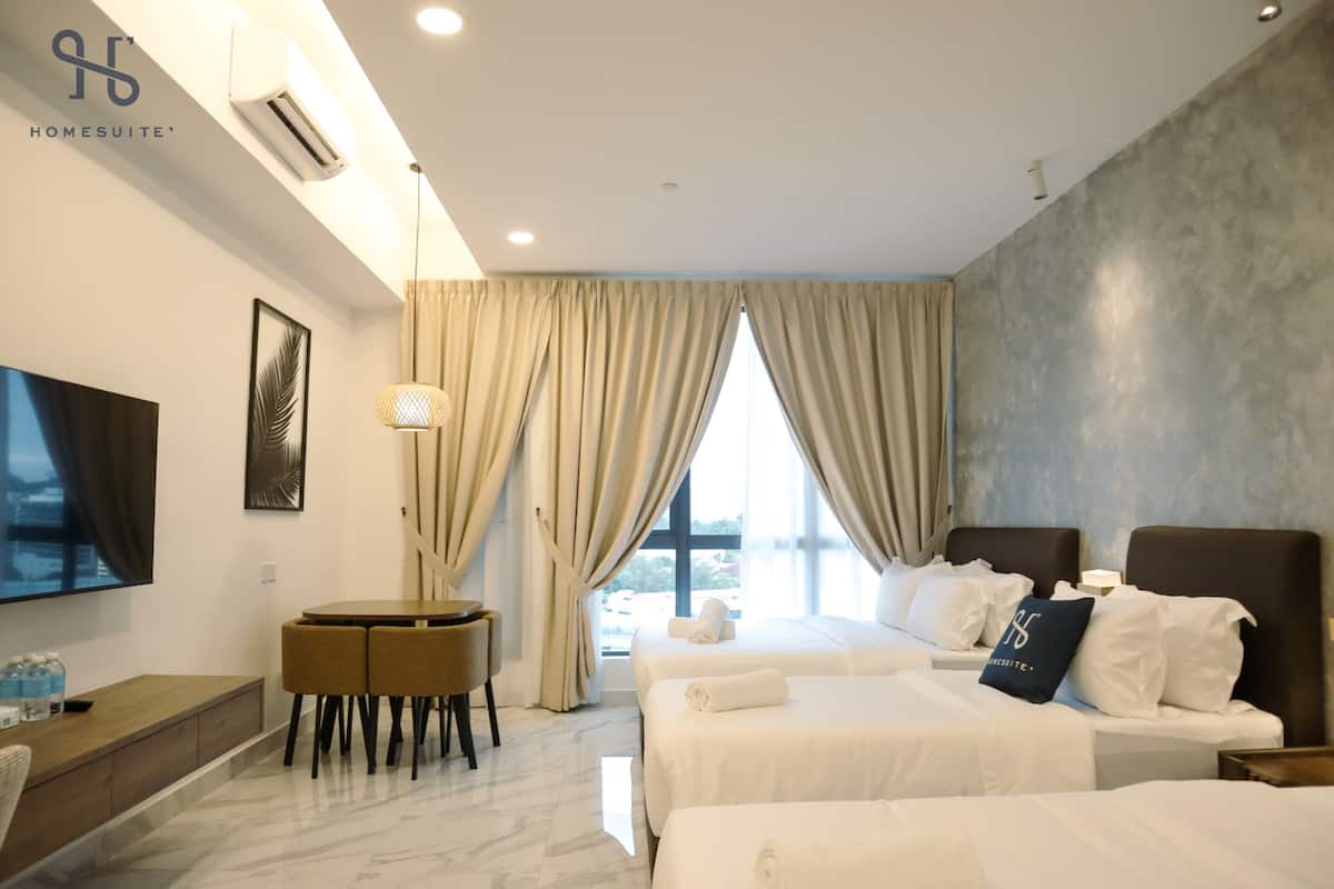 Quarto de hotel com duas camas, televisão, escrivaninha e vista para o exterior.