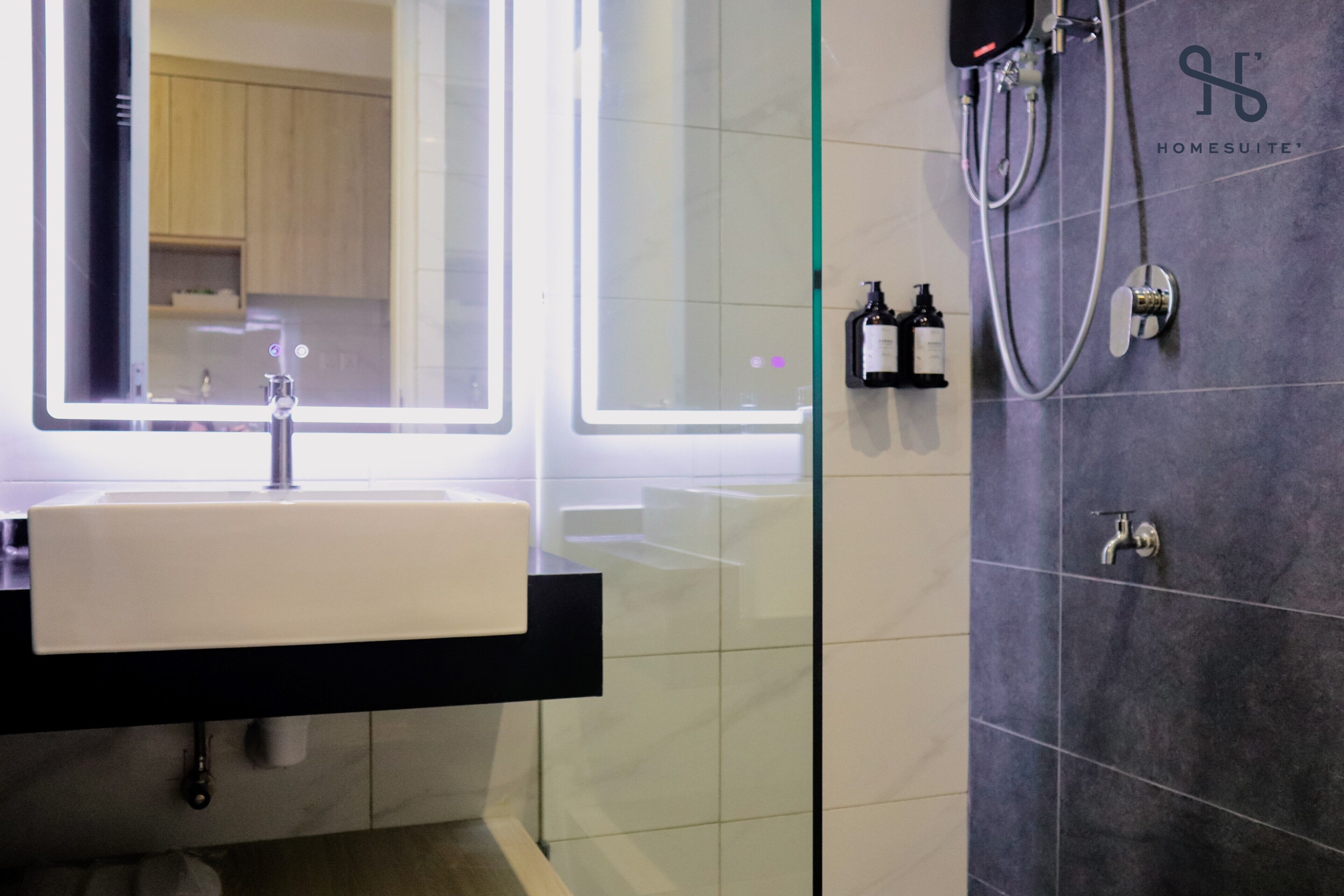 Une salle de bain moderne avec un grand miroir, un lavabo blanc et un espace douche doté d’un panneau de commande.