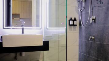 Une salle de bain moderne avec un grand miroir, un lavabo blanc et un espace douche doté d’un panneau de commande.