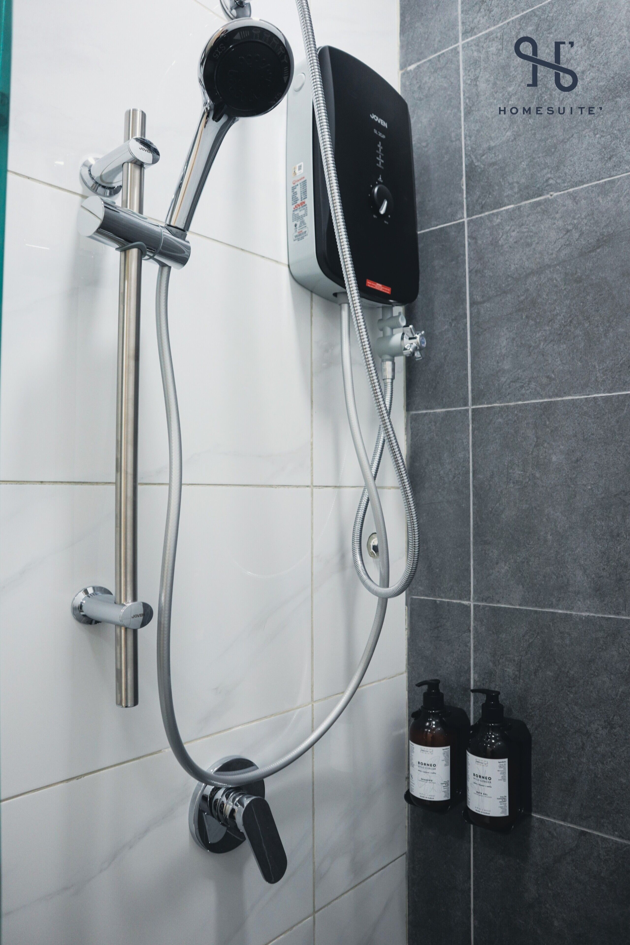 A shower with a handheld showerhead, a wall-mounted control panel, and two bottles of shampoo and conditioner on the wall.
