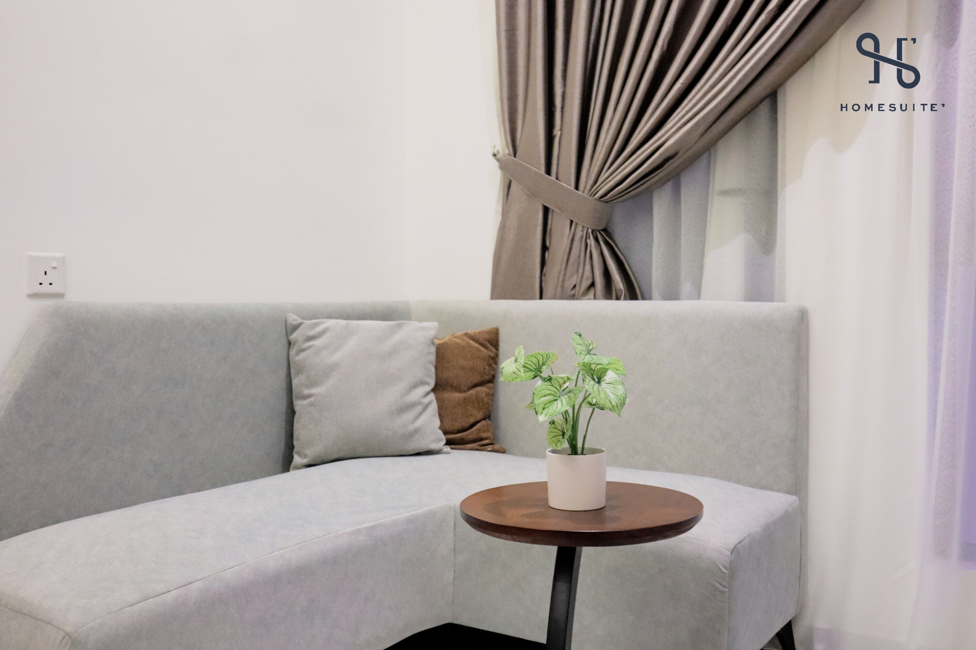 Ein modernes Wohnzimmer mit grauem Sofa, einem kleinen runden Tisch und einer Topfpflanze.