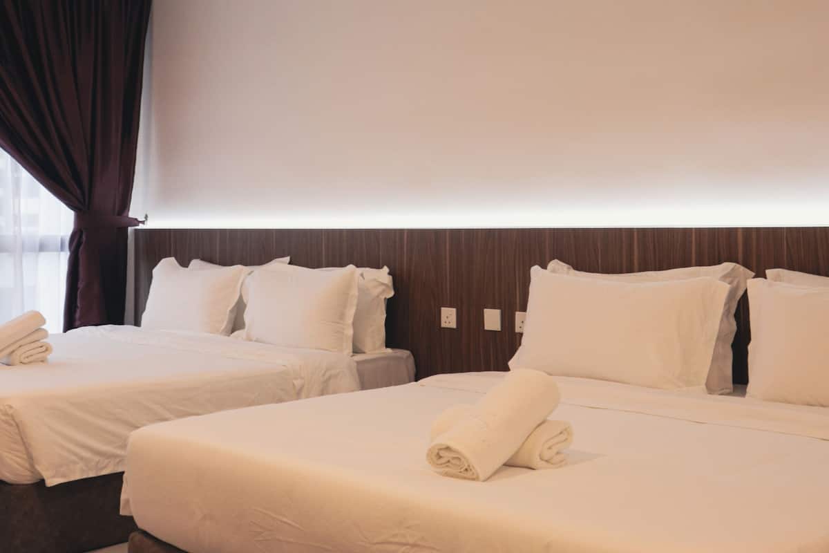 Quarto de hotel com duas camas, cada uma com lençóis e almofadas brancos, cabeceira de madeira e uma janela com cortinas.