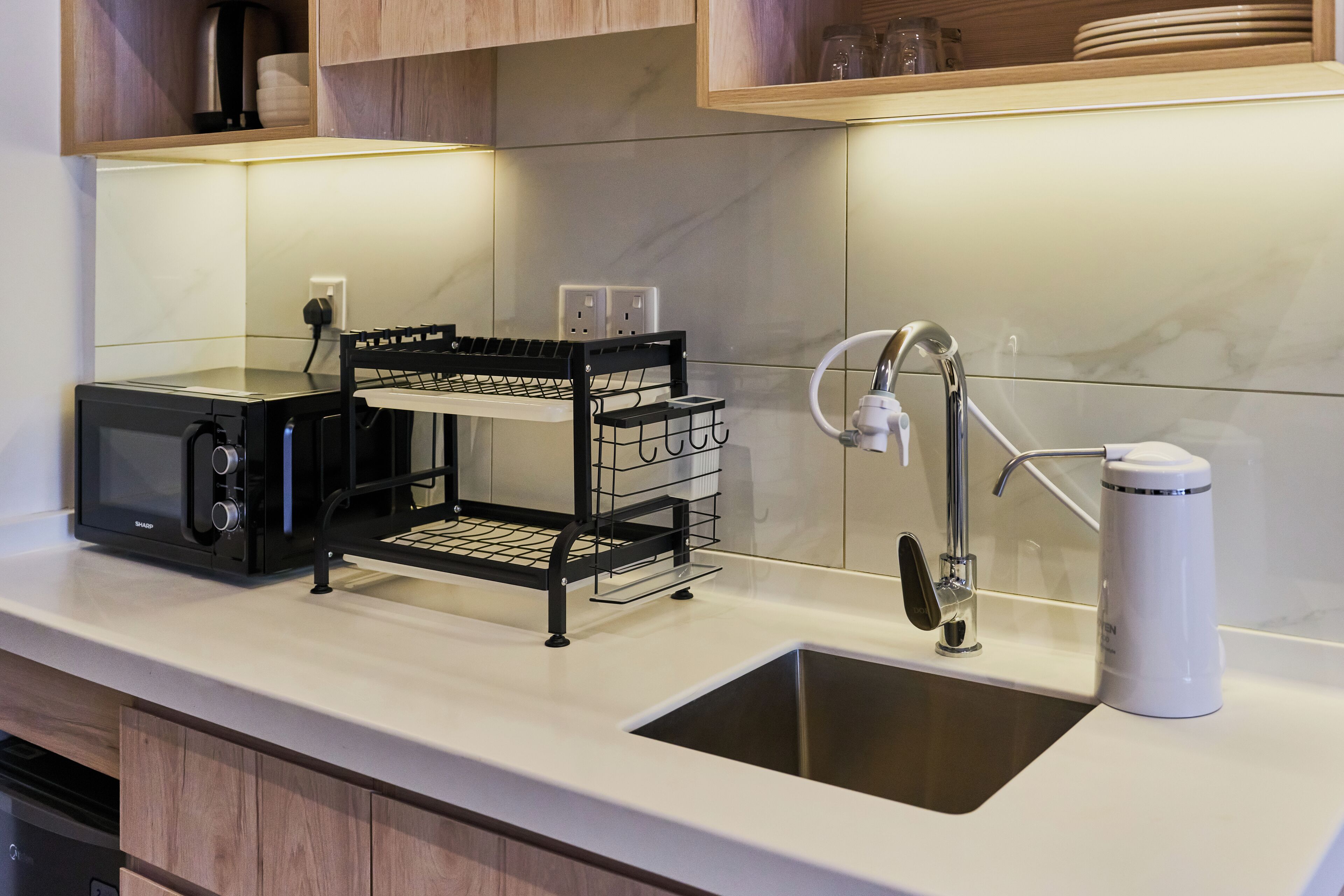 A kitchen with a built-in microwave, a black wire rack, a white coffee maker, and a stainless steel sink.