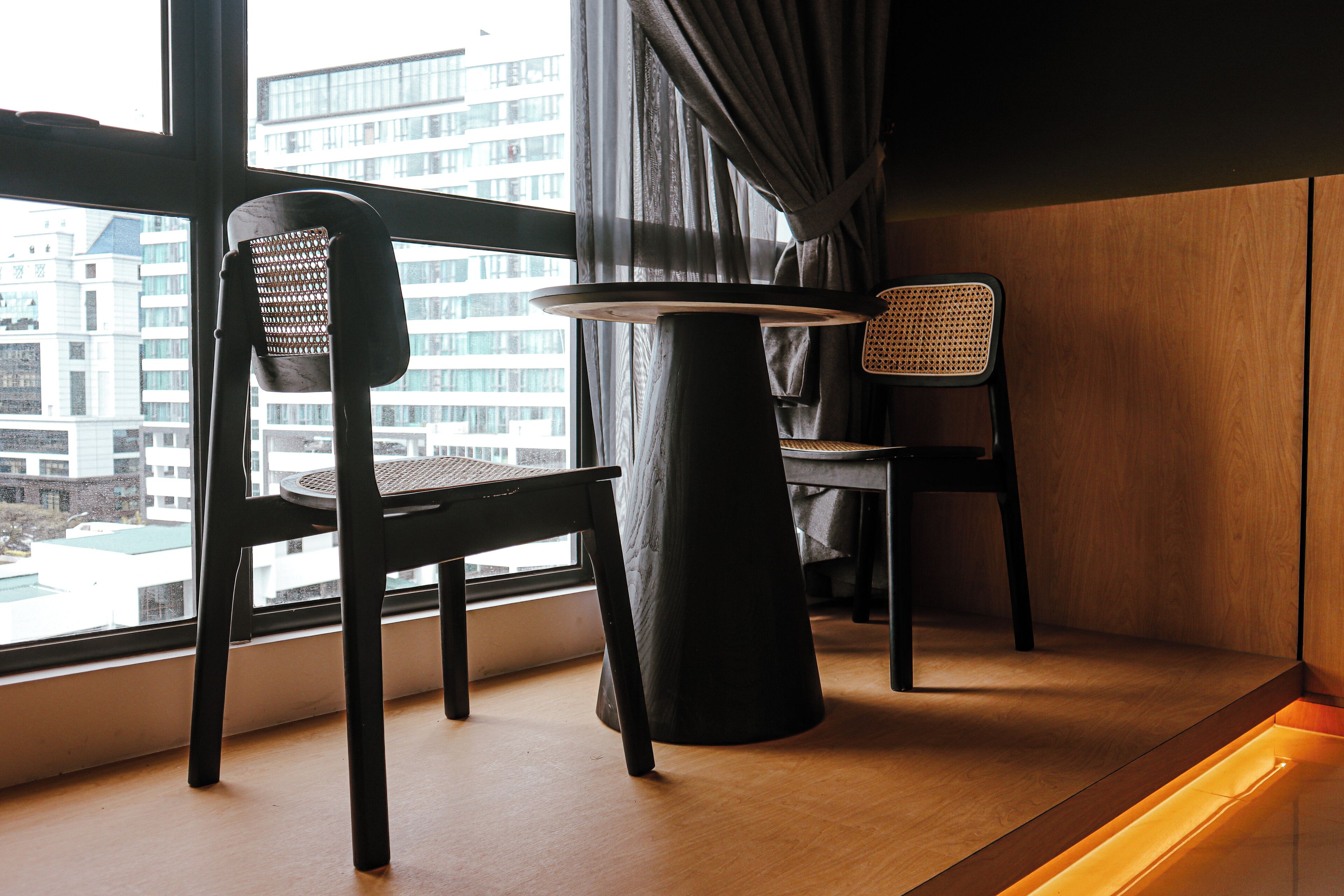 A modern room with a large window, two chairs, a round table, and a wooden floor.