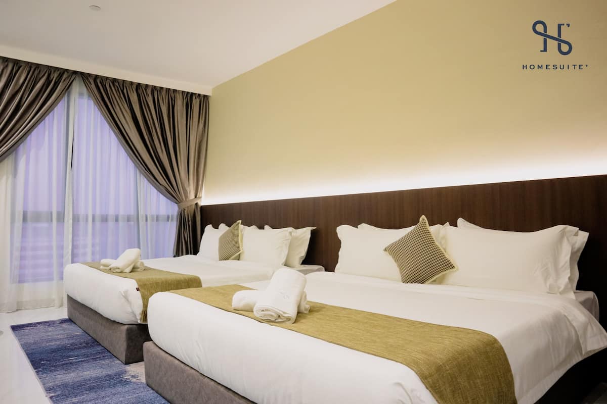 Quarto de hotel com duas camas, uma janela grande com cortinas e um logotipo na parede.