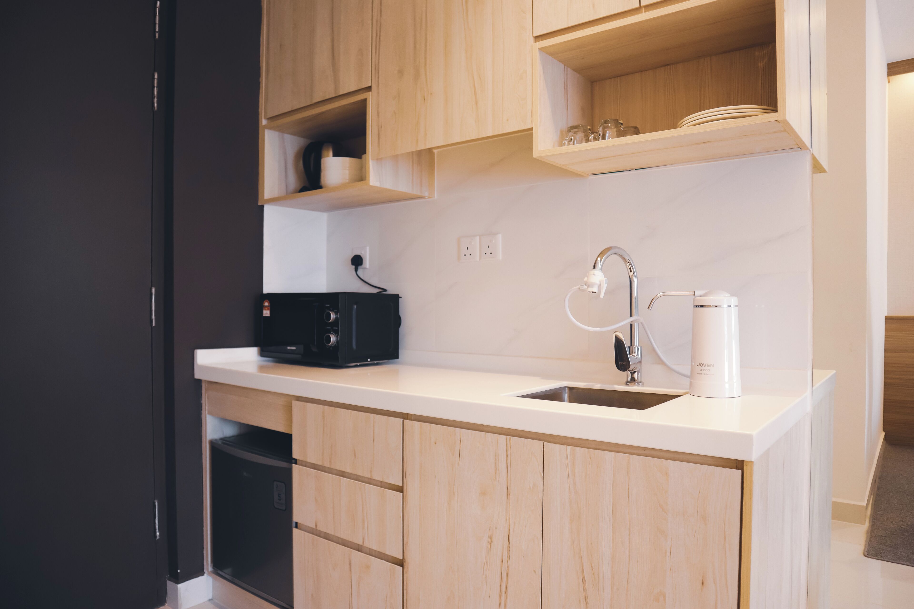 A modern kitchen with wooden cabinets, a white countertop, a black coffee maker, and a stainless steel sink.