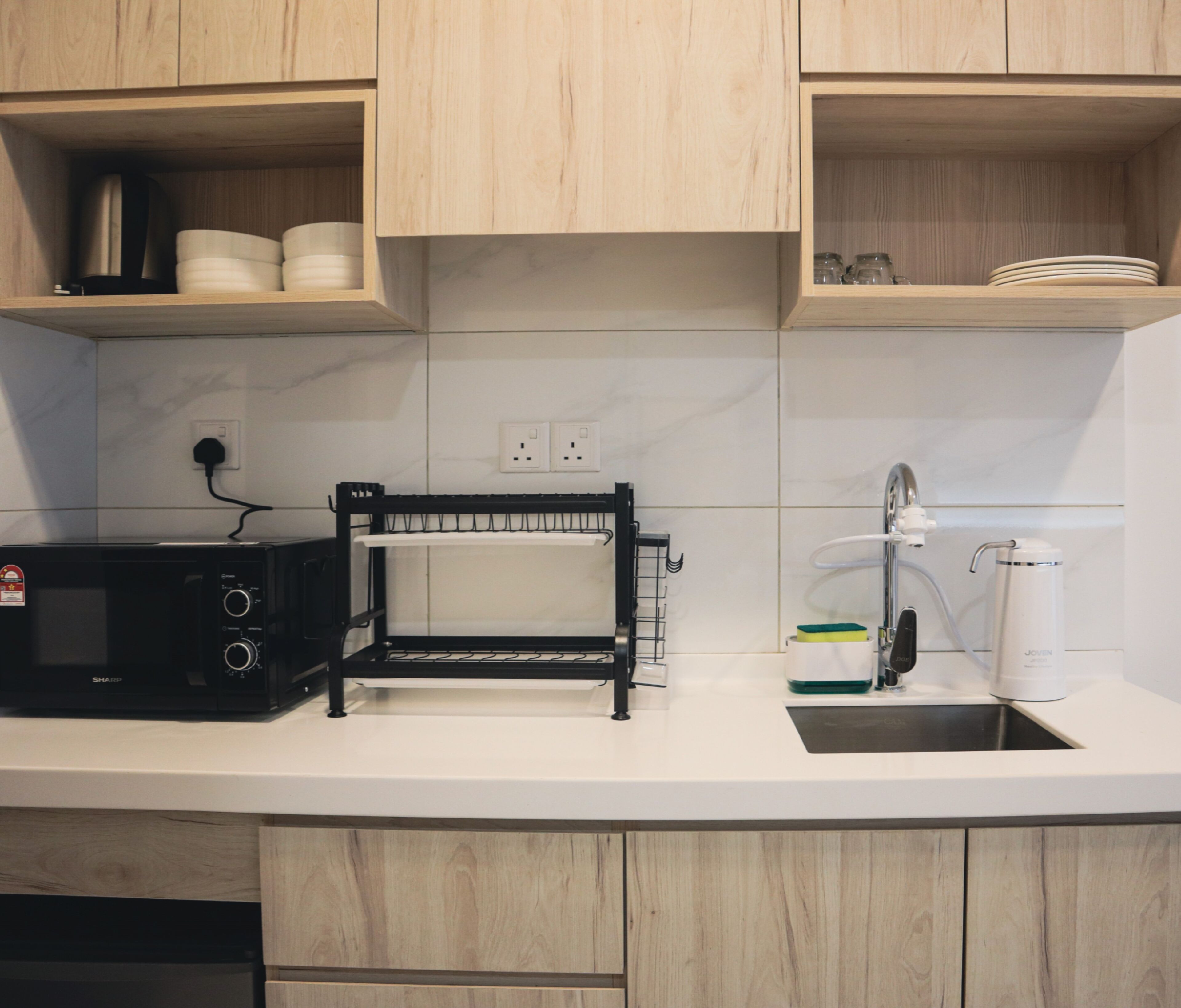 Una cocina con armarios de madera, microondas, tendedero, pileta y cafetera.