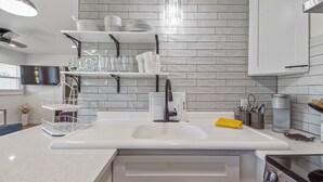 Une cuisine moderne avec des meubles blancs, un grand îlot central doté d’un évier et un revêtement mural en carreaux gris.