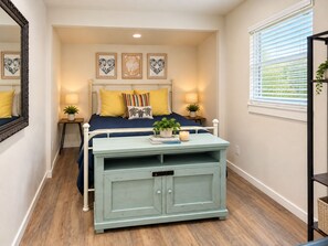 Une chambre à coucher comprenant un lit, des tables de chevet, une commode, un miroir et des œuvres d’art accrochées au mur.