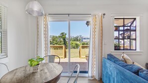 Une pièce avec une table en bois, un canapé bleu, une plante en pot et une vue sur un jardin et une maison, visible à travers une porte-fenêtre coulissante.