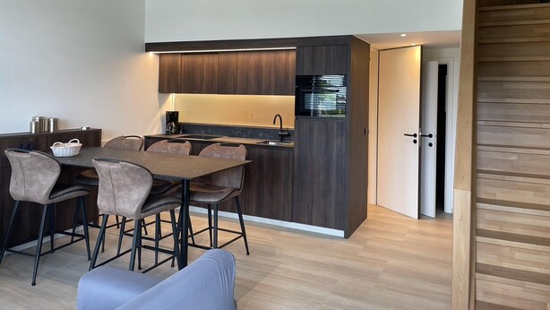 Una cocina moderna con armarios de madera oscura, horno empotrado y comedor con mesa y sillas.